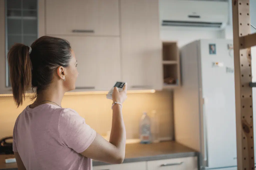 A young woman adjusting her air conditioning unit in the kitchen for optimal home comfort.