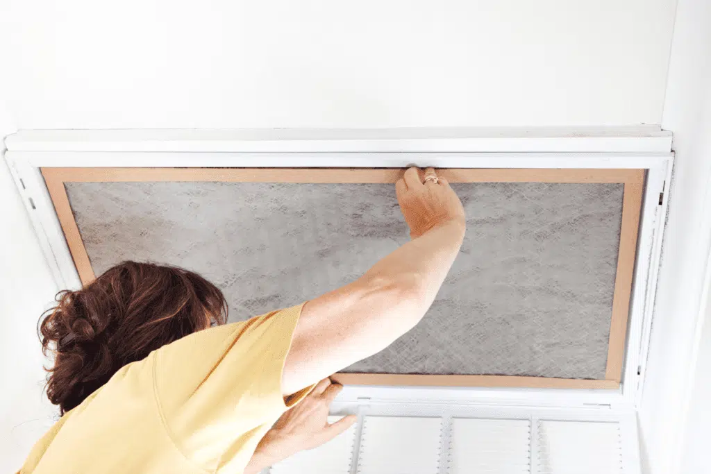 A woman replacing the air filter in an overhead vent to improve indoor air quality and HVAC efficiency.