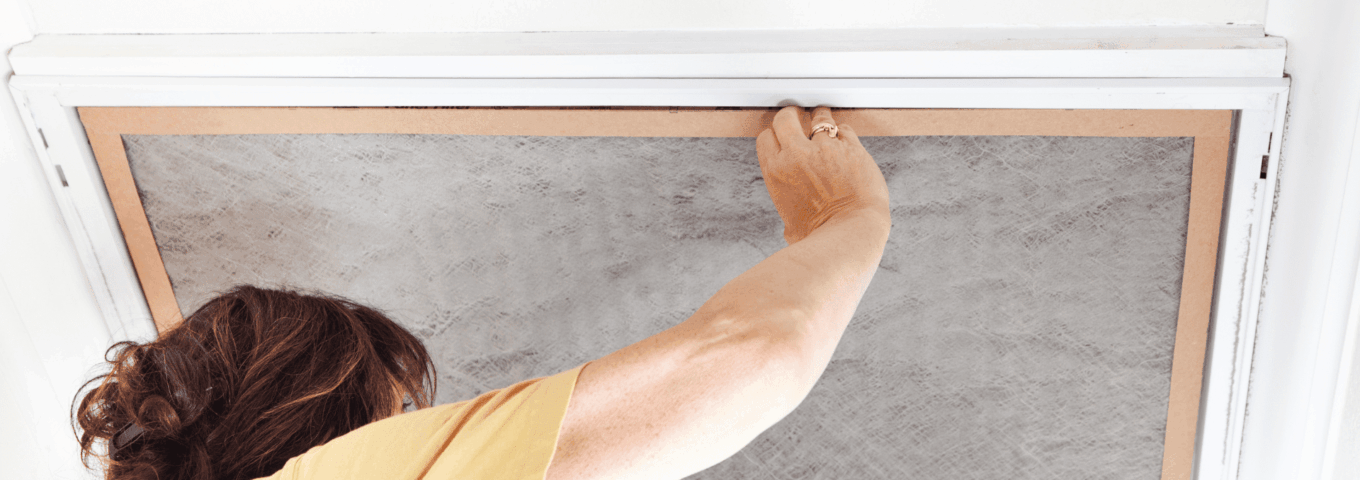 A woman replacing the air filter in an overhead vent to improve indoor air quality and HVAC efficiency.