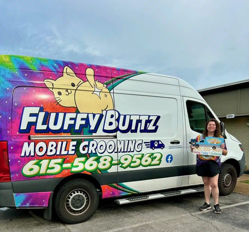 Person standing beside a colorful FluffyButtz Mobile Grooming van holding a Right Time HVAC sign.